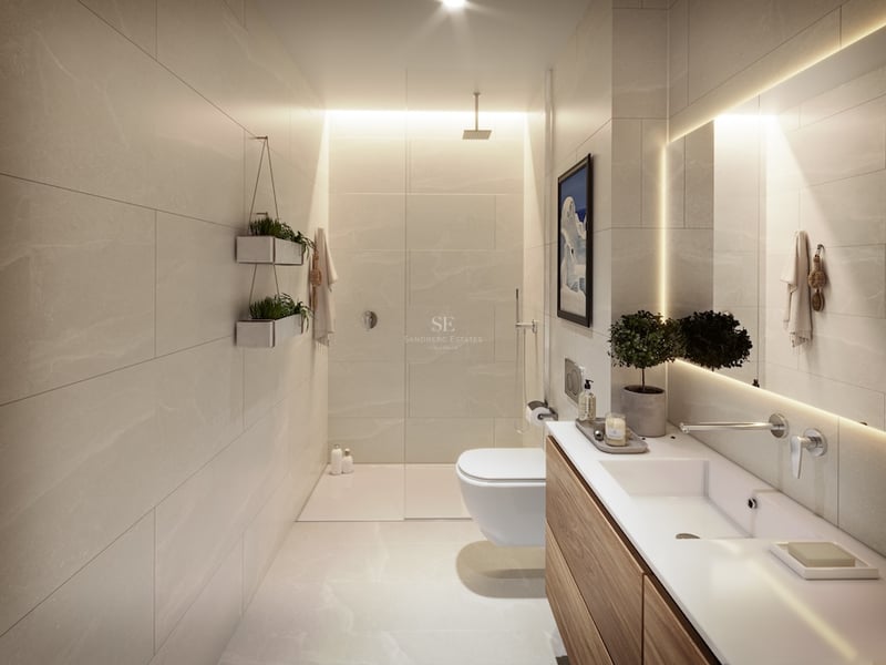 Modernt badrum med beige kakel, duschvägg i glas, träkommod och bakgrundsbelyst spegel.