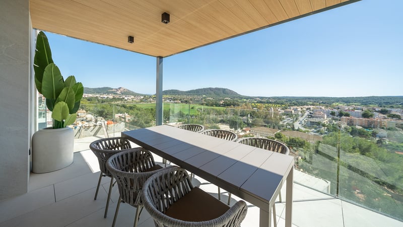 Terrasse couverte contemporaine avec table à manger pour six, garde-corps en verre et vue sur un village méditerranéen.