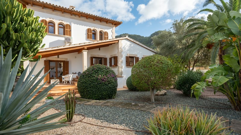 White Mallorcan-style villa with wooden shutters and a succulent garden set against a mountain backdrop.