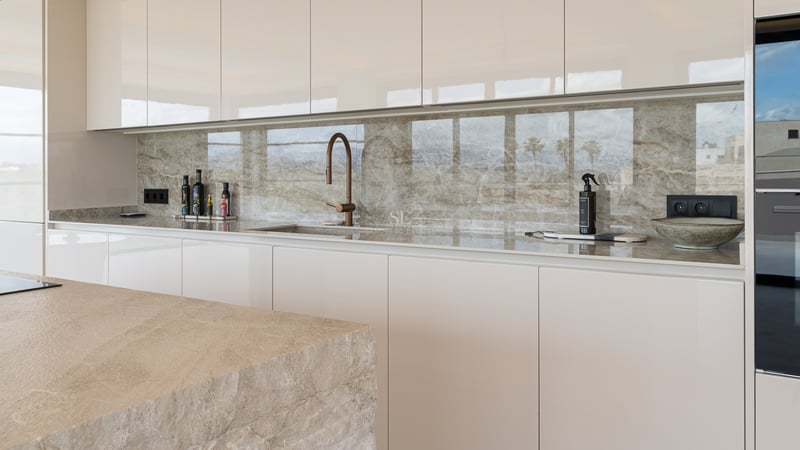 Moderne Küche mit cremefarbenen grifflosen Schränken, gemaserter Marmorrückwand und Design-Armatur in Bronze.