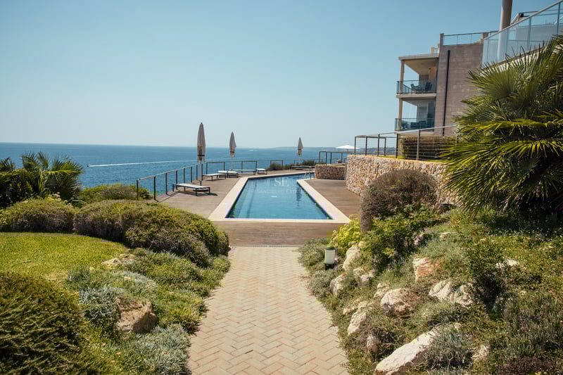 Longue piscine bordée d'une terrasse en bois surplombant la Méditerranée avec des jardins paysagers.