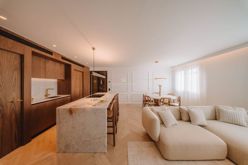 Espace moderne ouvert avec îlot en marbre, armoires en bois, parquet en chevrons et grand canapé beige.