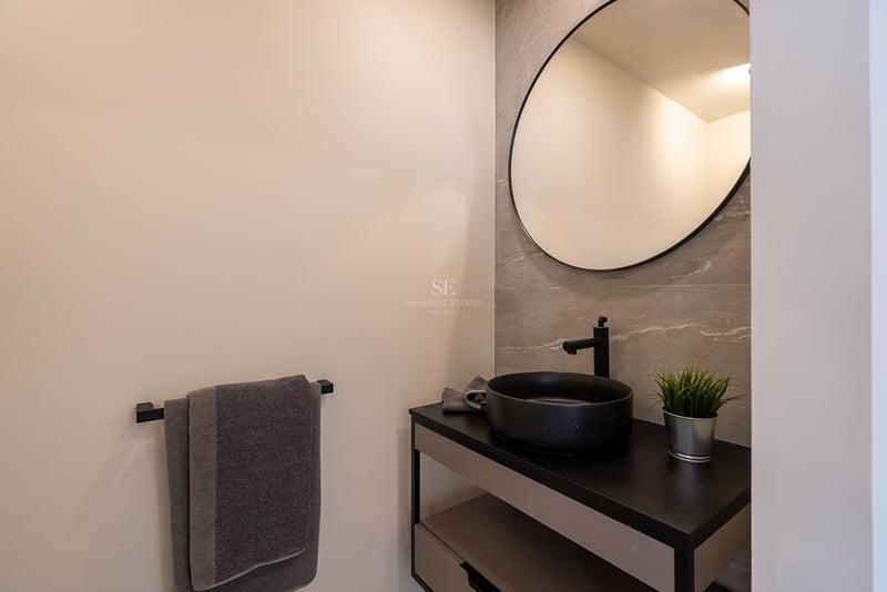 Modernes Badezimmer mit rundem Spiegel, schwarzem Aufsatzwaschbecken und grauen Fliesen in Steinoptik.