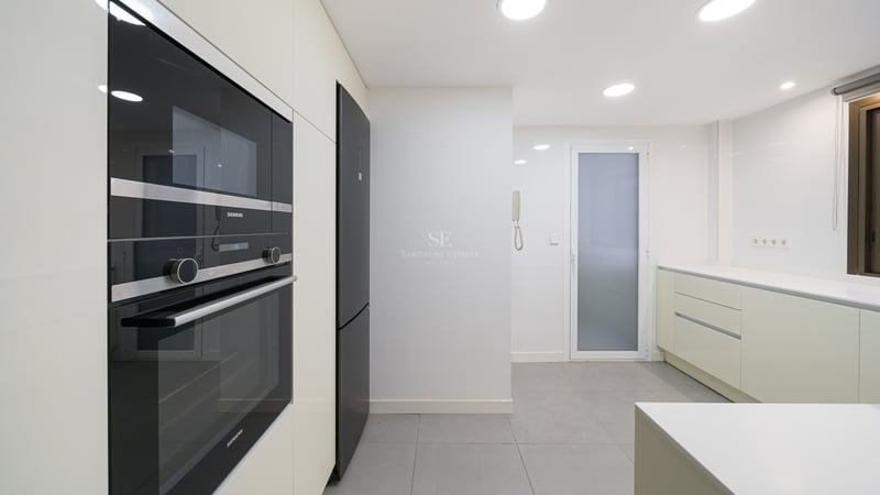 Modernt vitt kök med inbyggda svarta Siemens-vitvaror, grått klinkergolv och infälld belysning.