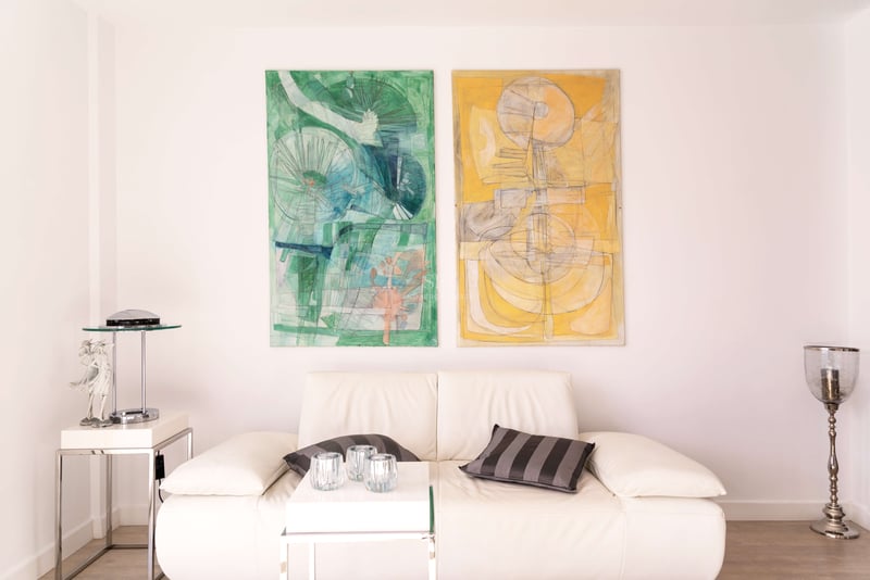 Weißes Ledersofa mit Chromakzenten neben zwei großen abstrakten Gemälden in Grün und Gelb an einer weißen Wand.