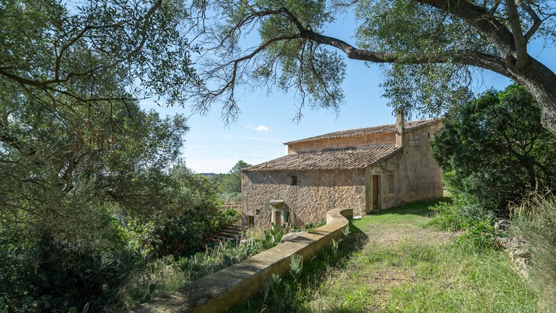 Une maison historique en pierre de deux étages avec un toit en terre cuite entourée d'arbres sous un ciel bleu.