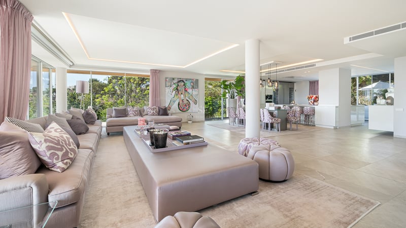 Großzügiger Wohnraum mit hellen Marmorböden, rosa Akzenten und bodentiefen Panoramafenstern zum Garten.