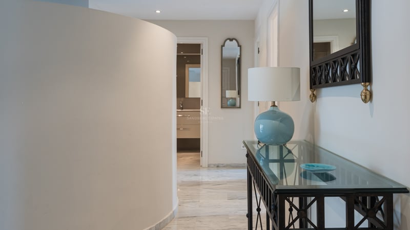 Modern entrance hall featuring a curved wall, polished marble floors, and a glass console table with a blue lamp.