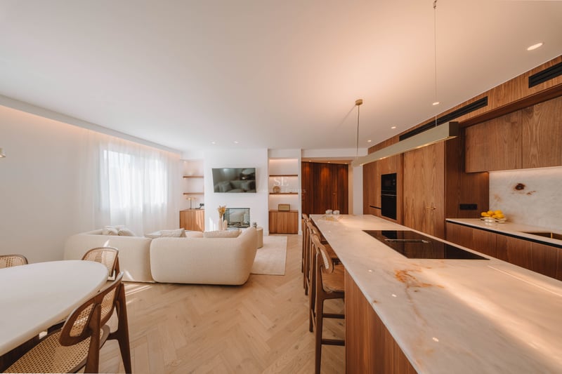 Espace de vie lumineux à concept ouvert avec un canapé beige, un îlot de cuisine en marbre et un parquet chaleureux.