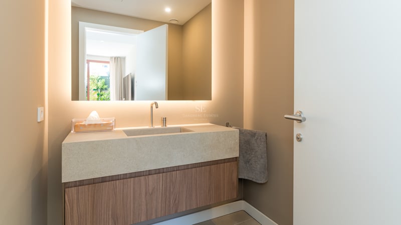 Contemporary bathroom vanity with a backlit mirror, stone countertop, and wood cabinetry in warm taupe tones.