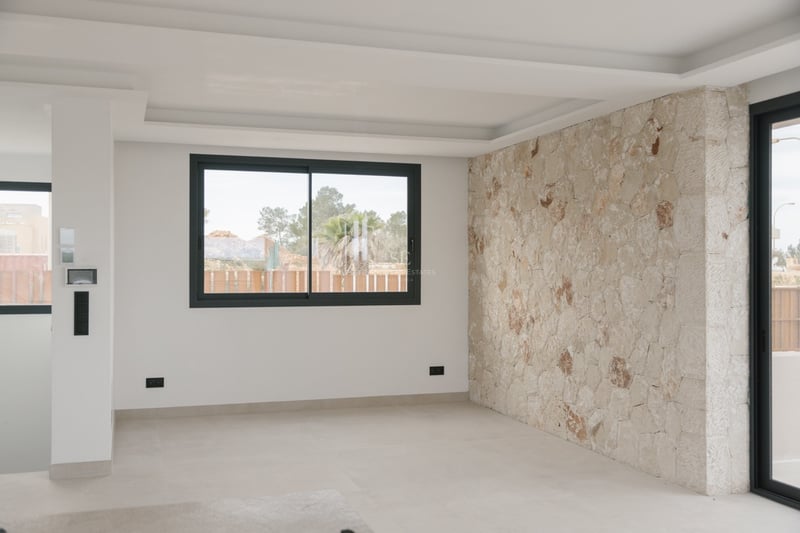 Leerer moderner Raum mit Natursteinwand, abgehängter Decke und schwarzen Aluminiumfenstern.