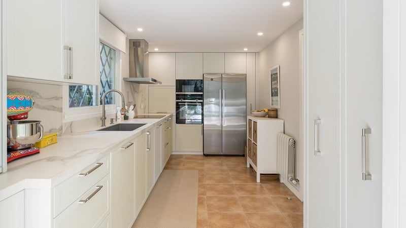 Contemporary galley kitchen featuring white cabinetry, marble countertops, stainless steel appliances, and terracotta floors.