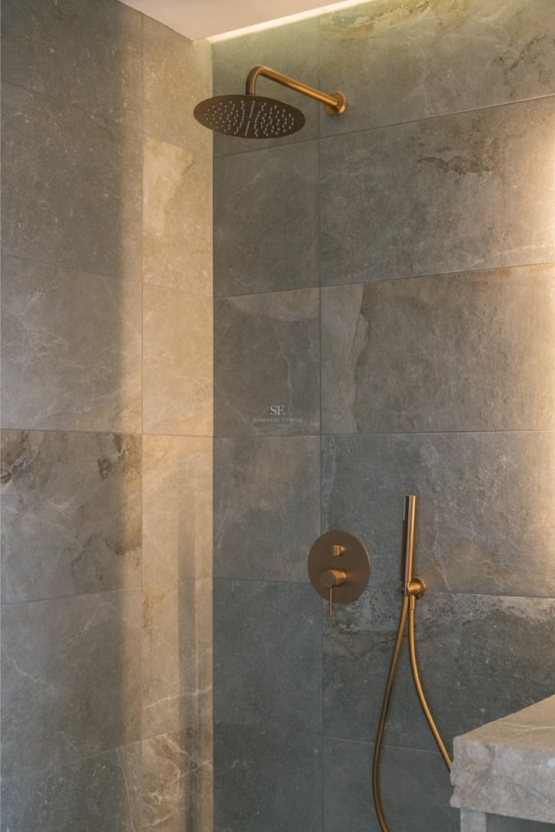 Luxuriöse Dusche mit großformatigen Natursteinfliesen und Regendusche in gebürstetem Messing mit LED-Lichtleiste.