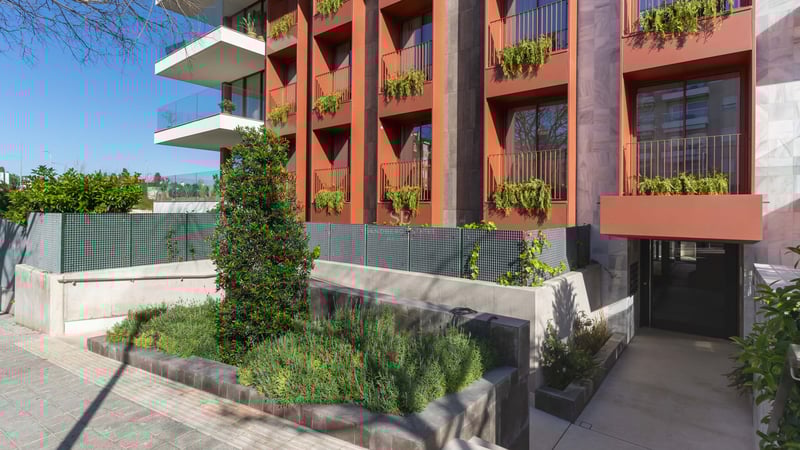 Exterior view of a modern multi-story building featuring terracotta panels, glass balconies, and integrated planters.