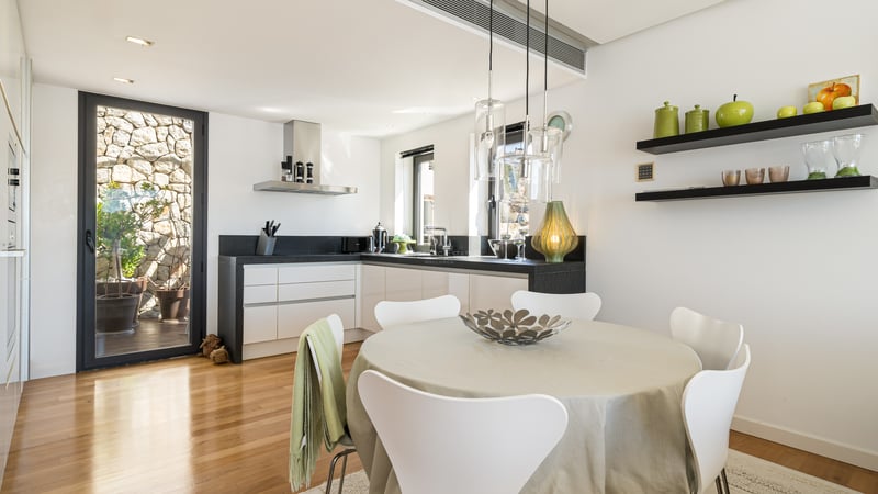 Bright kitchen with white cabinetry, black countertops, wooden floors, and a round dining table.