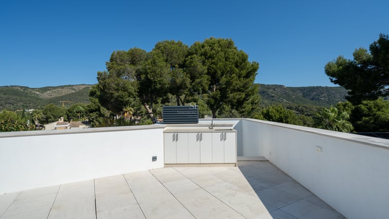 Toit-terrasse aux murs blancs avec une kitchenette extérieure intégrée donnant sur des collines verdoyantes.