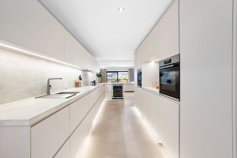 Cuisine moderne avec placards blancs sans poignées, plans de travail en marbre et éclairage LED intégré.