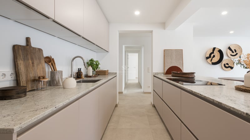 Modern kitchen with beige cabinets, stone countertops, and a view down a white hallway.