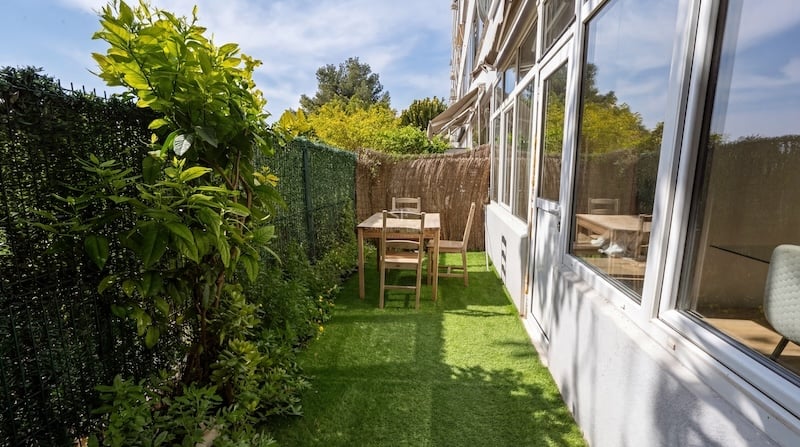 Terraza exterior estrecha con césped artificial verde, conjunto de comedor de madera y vallas de privacidad.