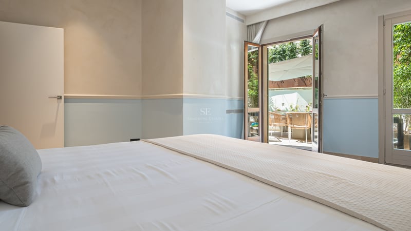 Chambre lumineuse avec linge de lit blanc et murs bleu clair s'ouvrant sur une terrasse ensoleillée.