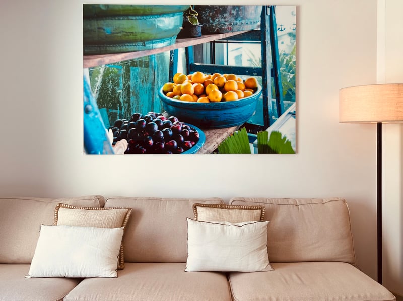Canapé beige avec coussins décoratifs sous une grande peinture sur toile de fruits dans des bols bleus.