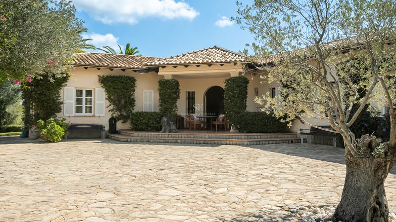 Villa méditerranéenne crème avec toit en terre cuite, volets blancs et une grande cour en pierre naturelle.
