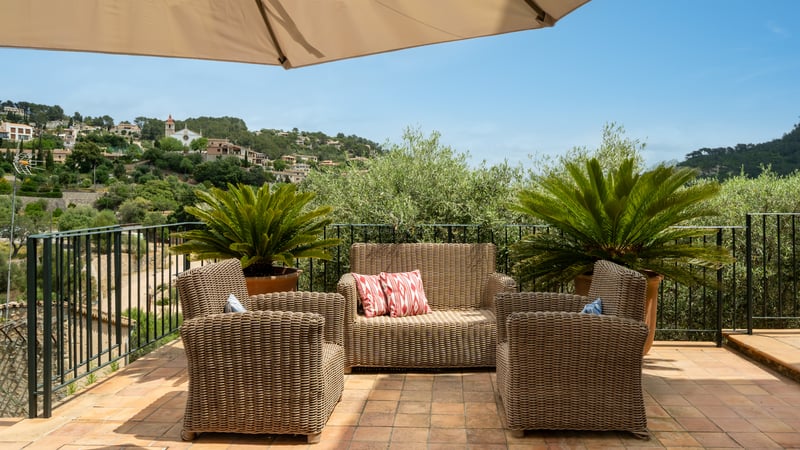 Salon de jardin en osier sur une terrasse en terre cuite avec vue sur les collines méditerranéennes et des villas.