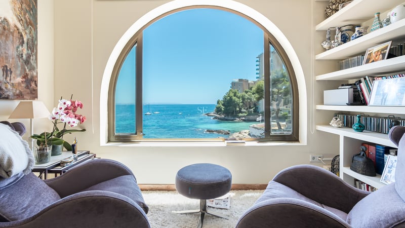 Två sammetsfåtöljer framför ett stort bågfönster med utsikt över en blå medelhavsvik med båtar.