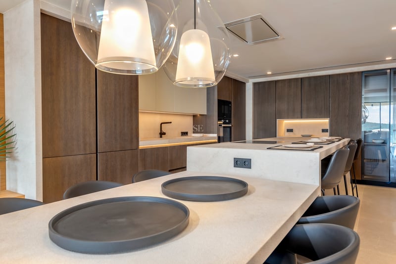 Cuisine moderne avec placards en bois sombre, îlot en pierre claire avec taburetes et suspensions en verre.