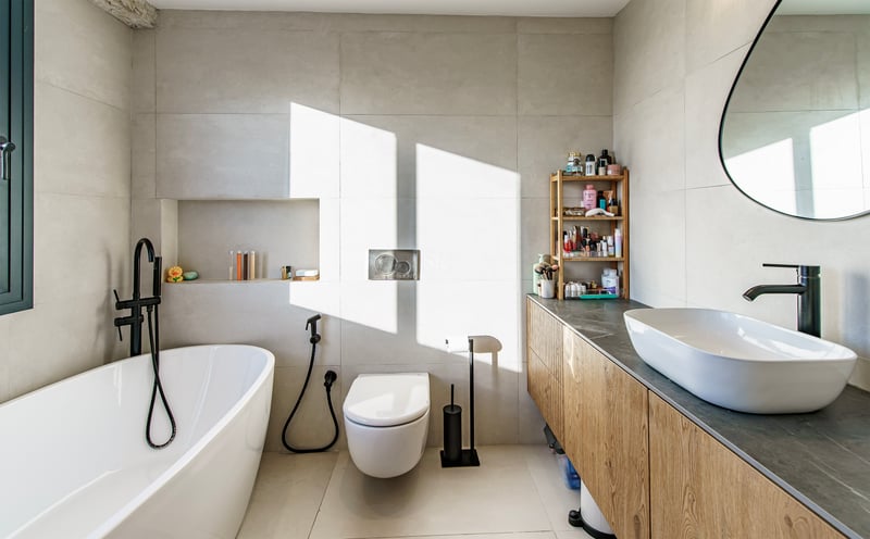 Salle de bain moderne et lumineuse avec baignoire îlot blanche, meuble sous vasque en bois et robinetterie noir mat.