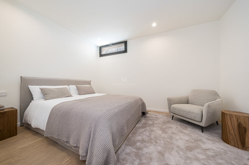 Modern bedroom featuring a double bed, grey armchair, natural wood side tables, and light oak floors.
