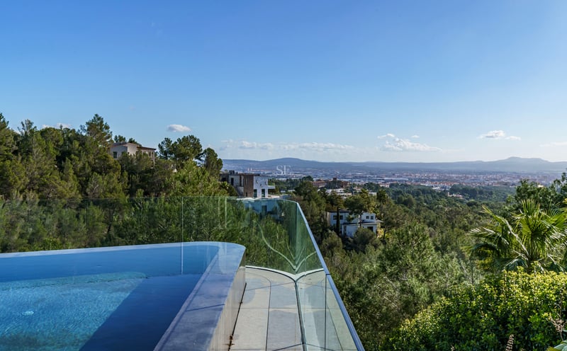 Piscine à débordement avec garde-corps en verre surplombant une vallée boisée et une ville lointaine.