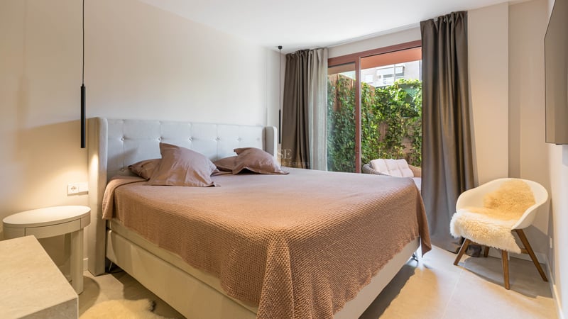 Modern bedroom featuring a king-size bed, glass sliding doors opening to a green patio, and contemporary pendant lighting.