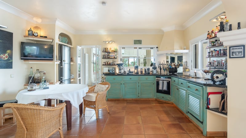 Cuisine méditerranéenne avec placards turquoise à persiennes, sol en terre cuite et coin repas en osier.