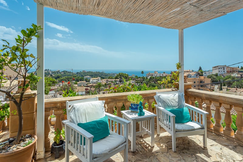 View of a modern villa with an infinity pool, stylish sun loungers, and minimalist architecture. Lush garden and blue sky in the background.