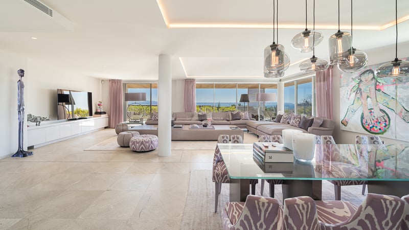 Großzügiges offenes Wohnzimmer mit modernen Polstermöbeln, Esstisch und Panoramafenstern zum Meer.