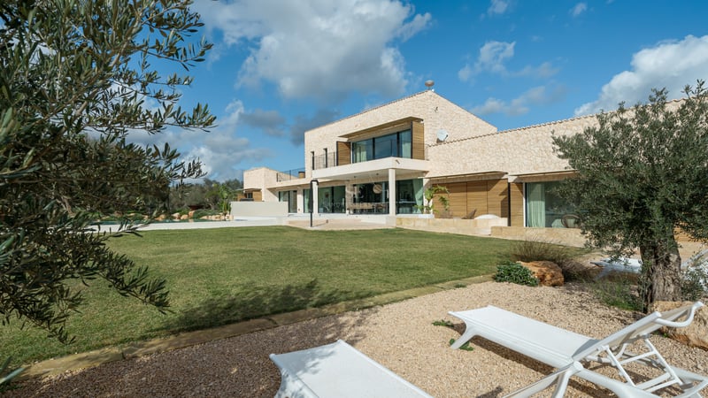 Samtida tvåvåningsvilla med naturstensväggar, stora glaspartier och gräsmatta under en blå himmel.
