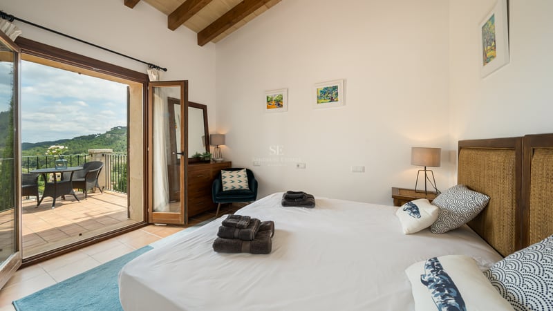 Chambre lumineuse avec poutres en bois, literie blanche et porte vitrée donnant sur une terrasse.