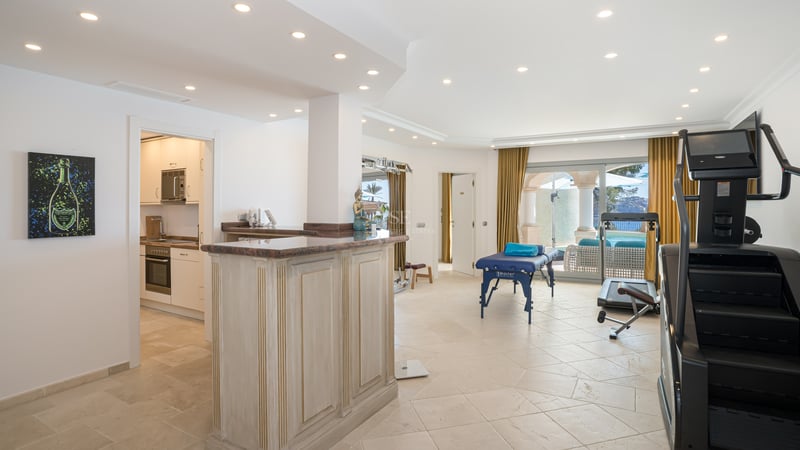 Heller Wellnessraum mit Massagetisch, Fitnessgeräten, Holzbar und Zugang zur Terrasse.