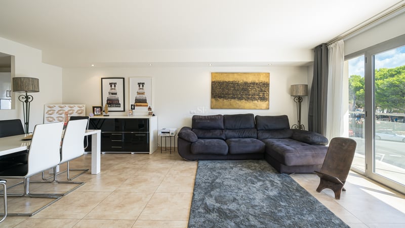 Rymligt modernt vardagsrum med mörk soffa, vit matgrupp och stora glaspartier med naturligt ljus.