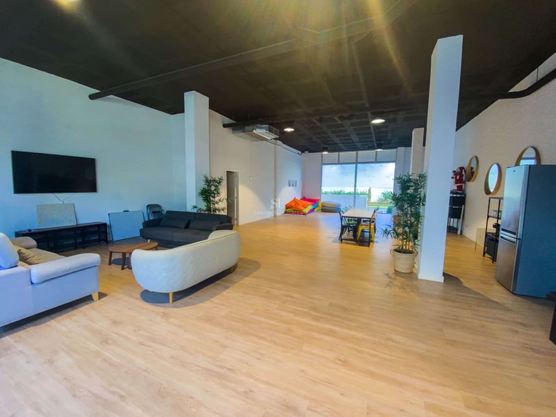 Großer offener Raum mit hellem Holzboden, Sofas, Esstisch, bunten Sitzsäcken und Zugang zum Garten.