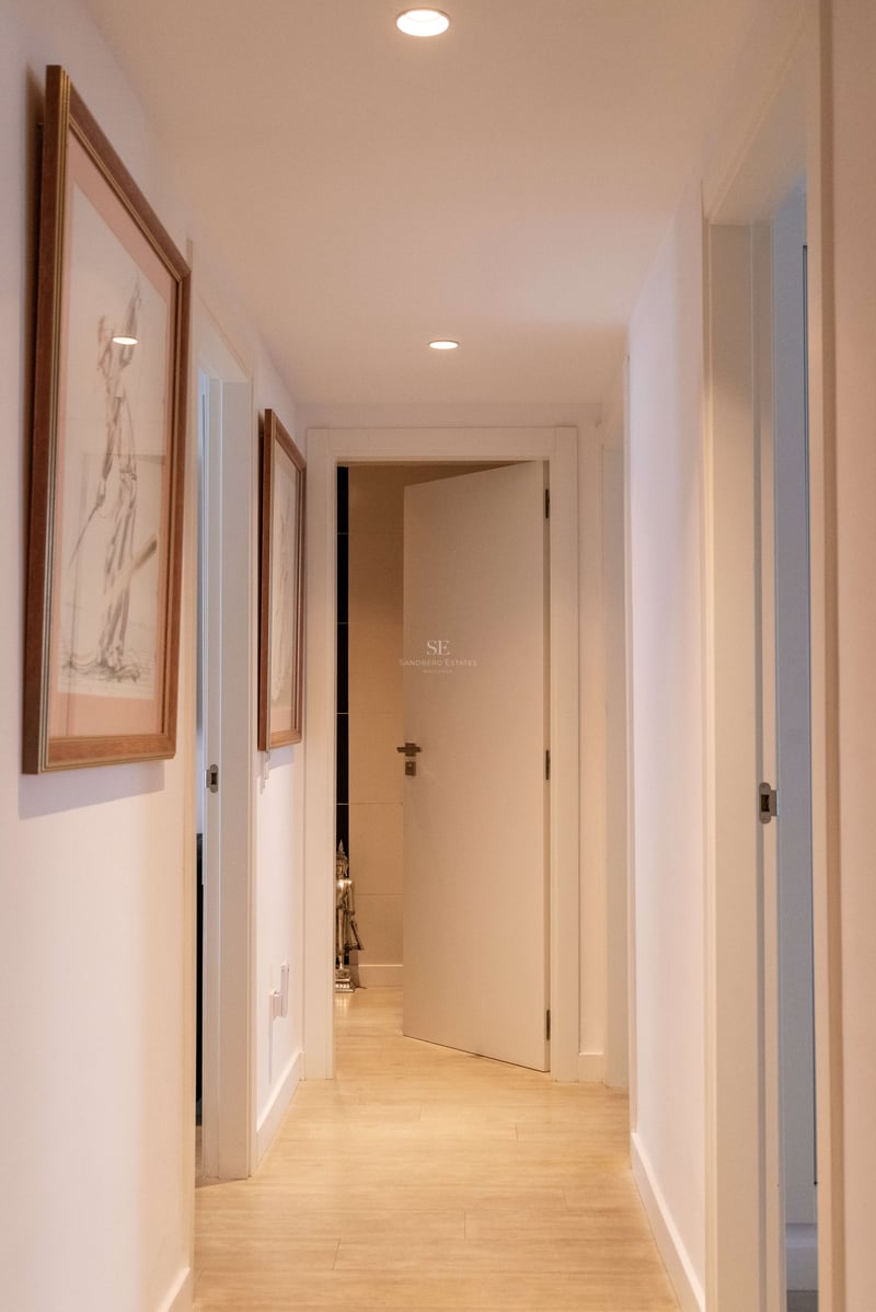 Moderner weißer Flur mit Einbaustrahlern und hellem Holzboden, der zu einer offenen Tür führt.