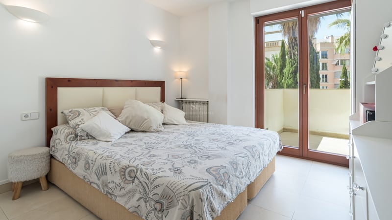 Chambre spacieuse avec lit double et accès direct à une terrasse privée bordée de palmiers.