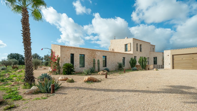 Naturstensfasad på en modern villa med kaktusträdgård och grusuppfart under en klarblå himmel.