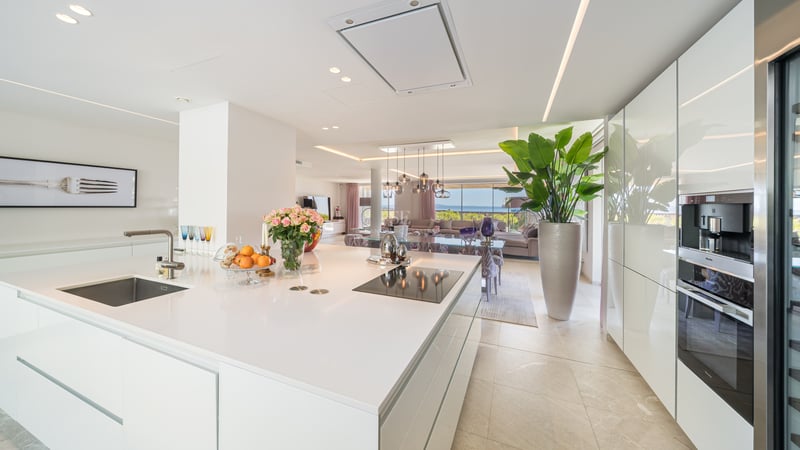 Weiße Kücheninsel mit Induktionskochfeld, mit Blick auf das Wohnzimmer und das Mittelmeer im Hintergrund.