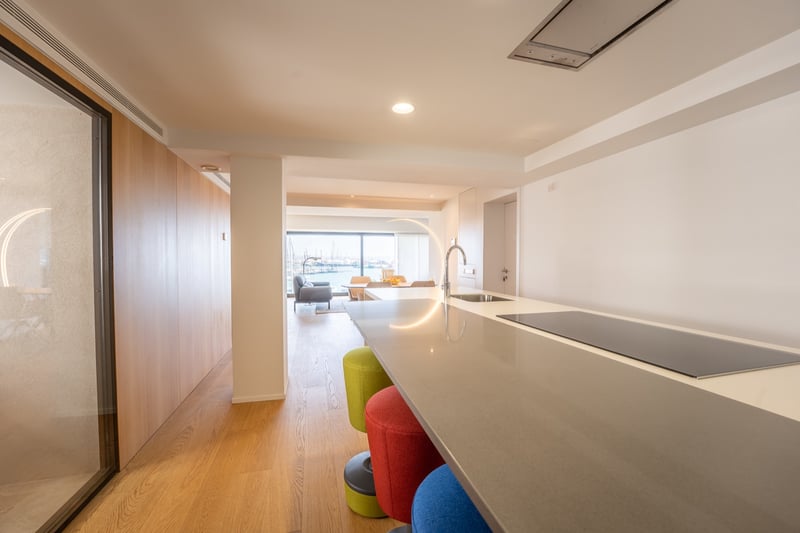 Köksö med färgglada pallar som leder till ett vardagsrum med utsikt över en marina genom fönster.