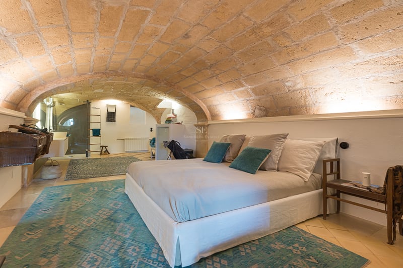 Chambre avec plafond voûté en grès, murs blancs, tapis turquoise et lit moderne.