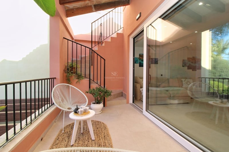 Terrass med terrakottafärgade väggar, vit Acapulco-stol, jutematta och spiraltrappa i järn.