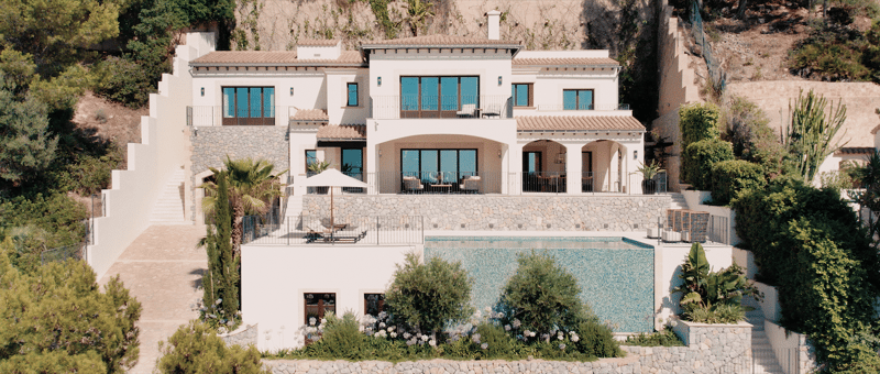 Exterior view of a multi-level white Mediterranean villa featuring a large infinity pool and stone accents.