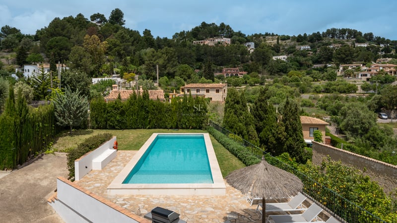 Piscine rectangulaire turquoise entourée d'une terrasse en pierre naturelle et de verdure avec vue sur la montagne.